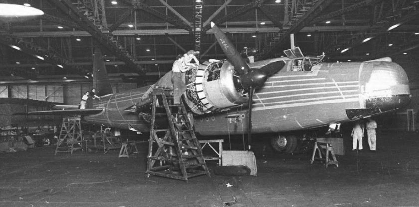 Photo of a bomber in mid production and an engineer working on the engine